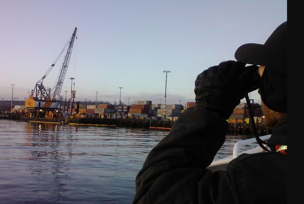 Man looking through binoculars at a shipping yard