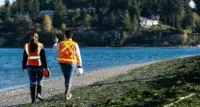 Two Farallon employees surveying a rocky beach with green seaweed.