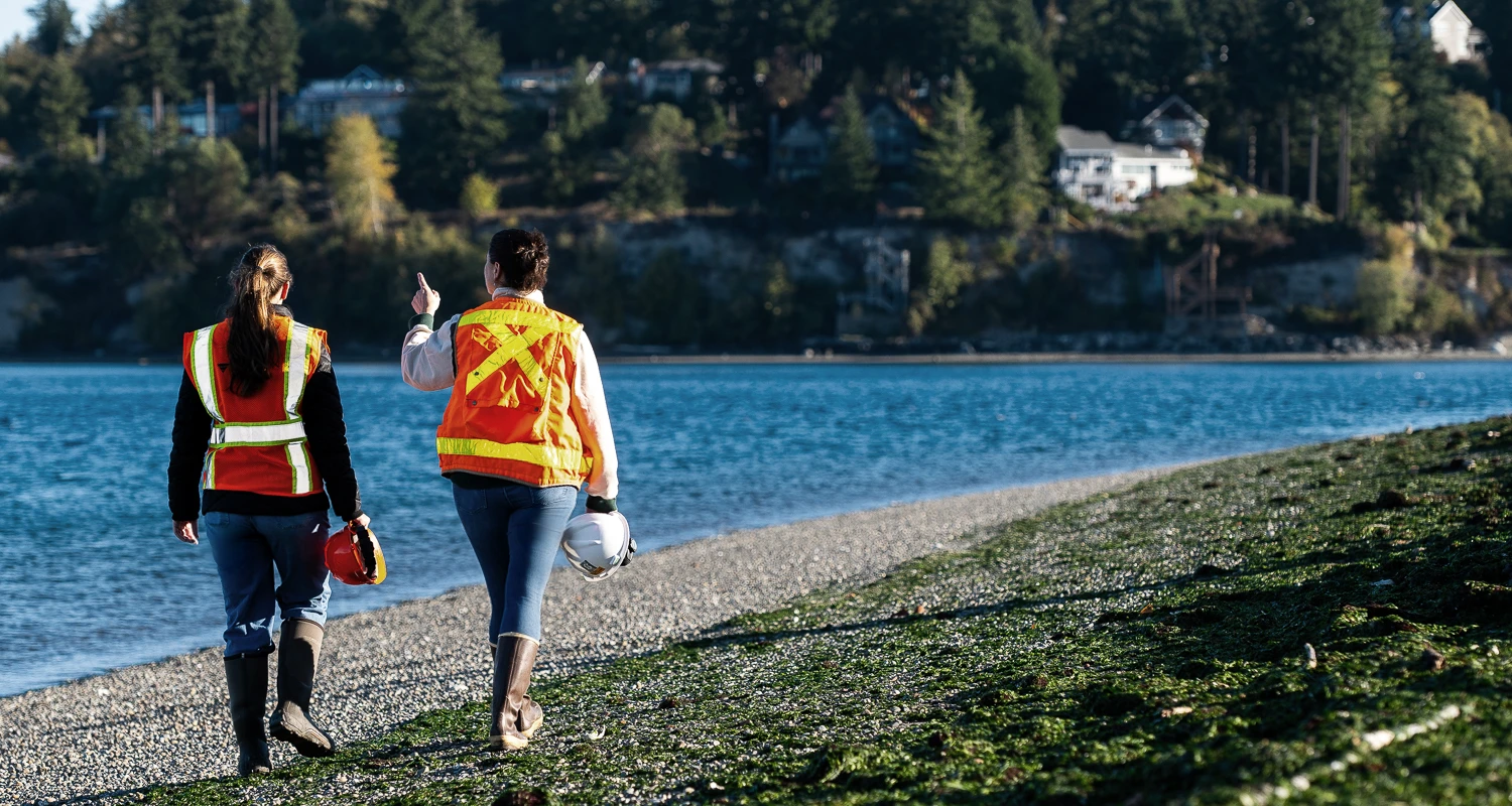 Two Farallon employees surveying a rocky beach with green seaweed.